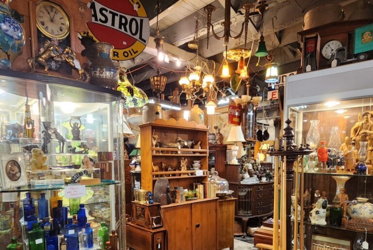 cluttered shelves full of antique trinkets and retro treasures are lit with many hanging antique lamps inside the antique alley store