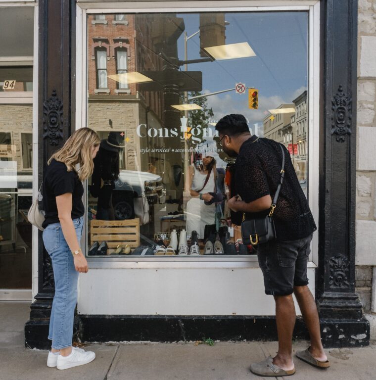 two shoppers admire the clothing arranged inside the storefront window from outside