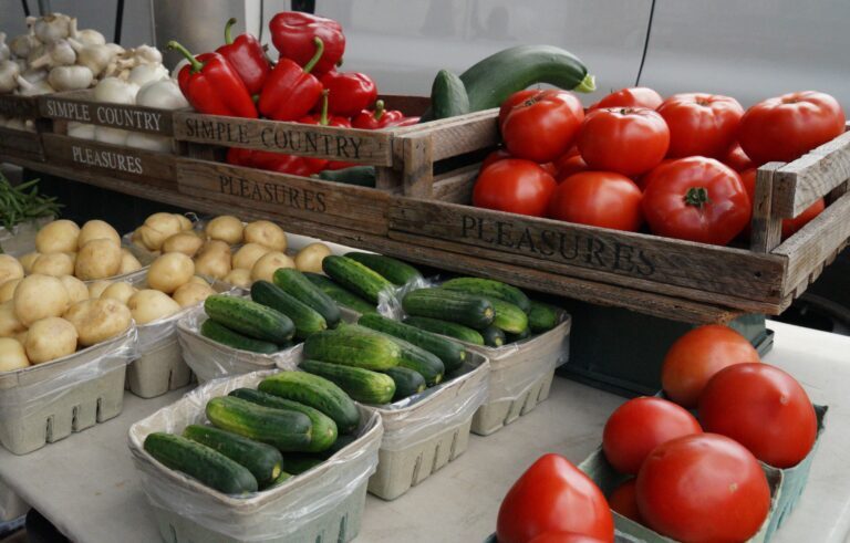 garlic heads, seasonal plump tomatoes, cucumbers, potatoes and red bell peppers sit in baskets on one of the simple pleasures market stalls tables