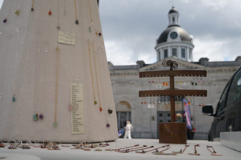 a close-up shot of elegant mineral rock pendants hung from a hand-made metal jewelry hanger, framed perfectly with city hall in the background