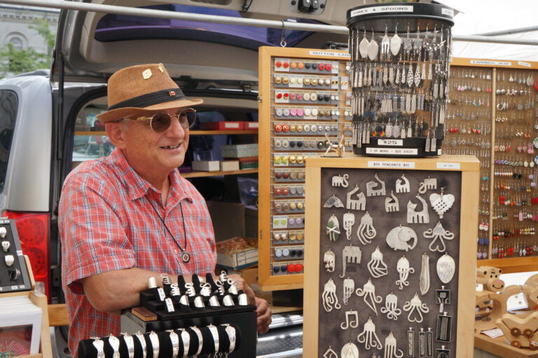 Iggy smiles inside his booth, proudly displaying his shiny creations which hang about his stall