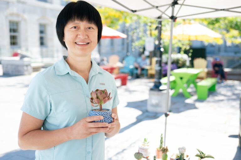 Angela poses happily with one of her many potted succulents in hand inside her market stall on a sunny day