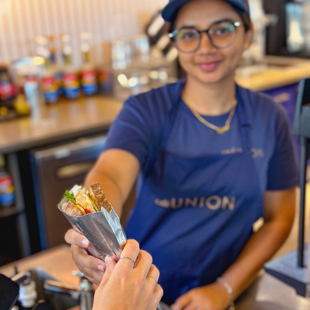 Cafe Union employee passing a sandwich