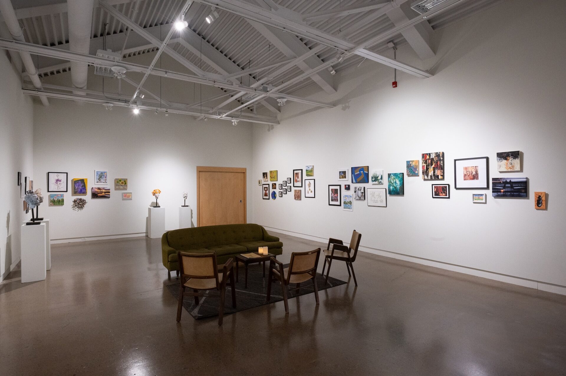 A big room with a couch and chairs in the middle with artwork hung up along the walls